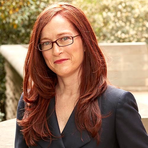 A woman with red hair and glasses is posing for a photo.